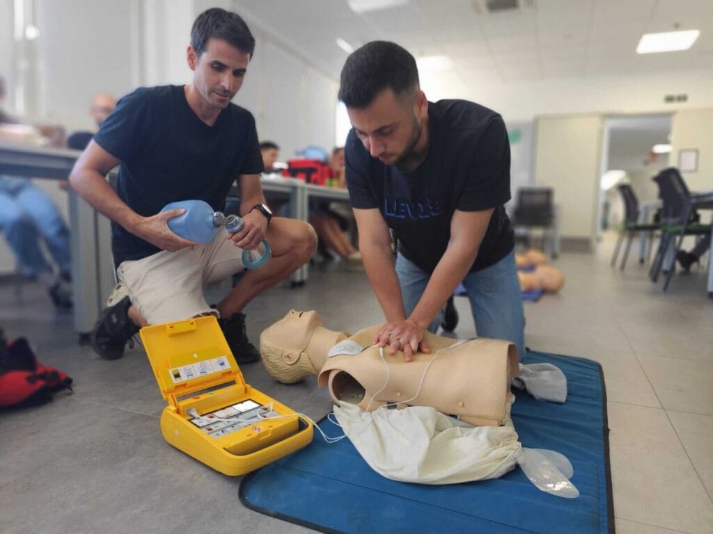 Dos empleados en un curso de desfibrilador para empresas impartido por Suma una Vida practicando RCP y uso de DESA con un maniquí