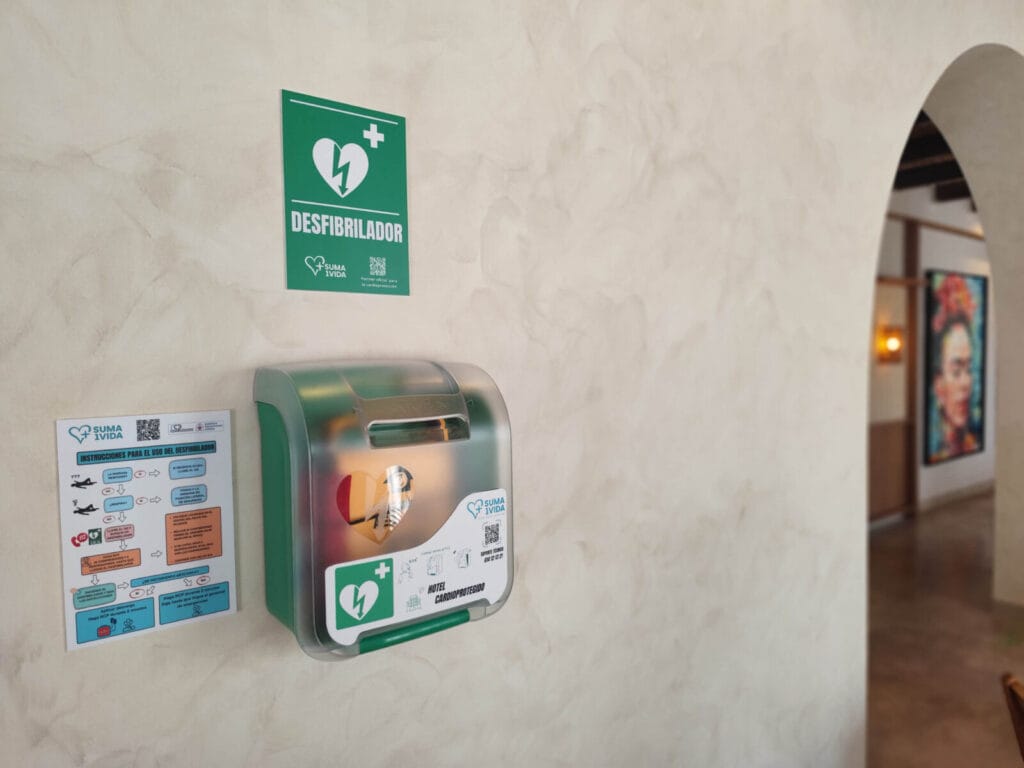 Desfibrilador externo semiautomático DEA instalado en la pared de un hotel junto a cartel de instrucciones de uso de Suma una Vida.