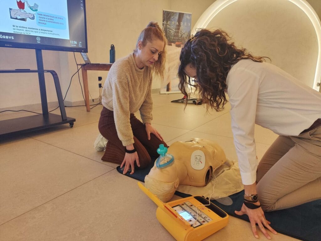 Dos trabajadoras de hotel aprendiendo a colocar los parches de un desfibrilador de entrenamiento en un maniquí de RCP durante un curso de primeros auxilios.